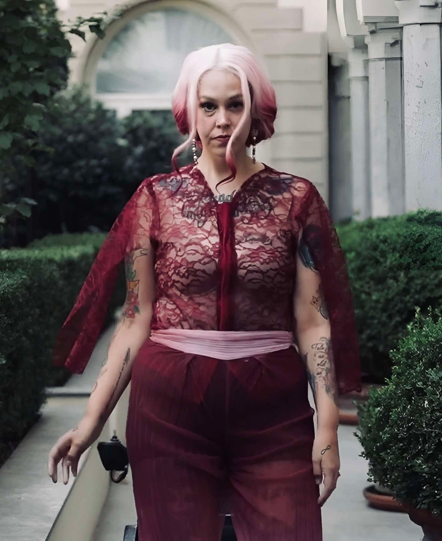 This photo shows a model wearing a top made of burgundy lace and cape sleeves