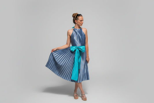 This photo shows a model wearing a size adjustable blue pleated dress with a teal waist belt from the front view