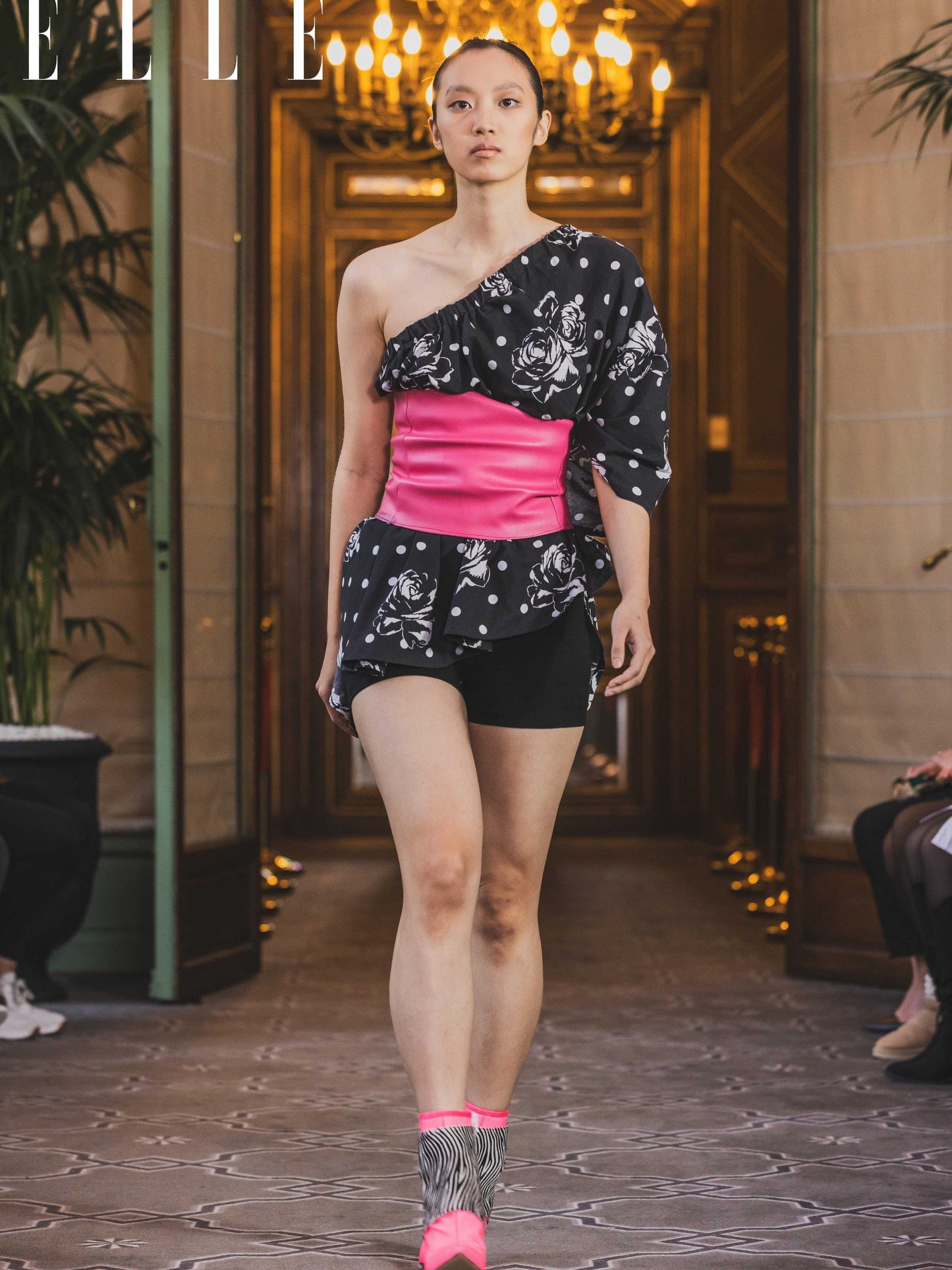 A model wearing a size adjustable black and white floral print top with a hot pink corset detail and corset backing for adjustability.