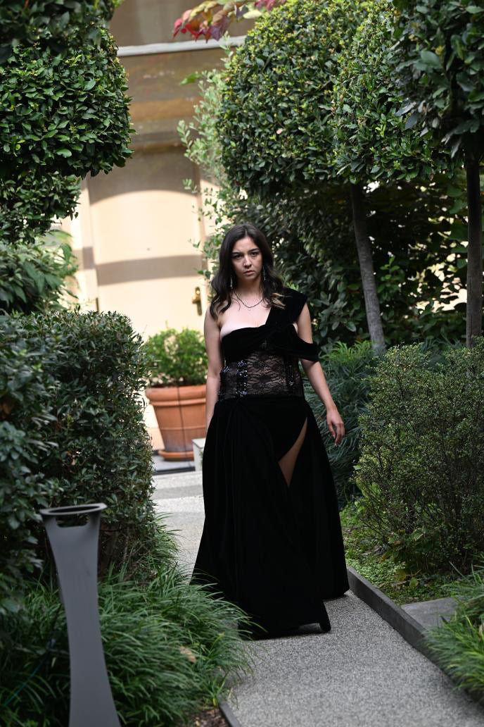 Black velvet floorlengt gown featuring a high slit and an off the shoulder sleeve.