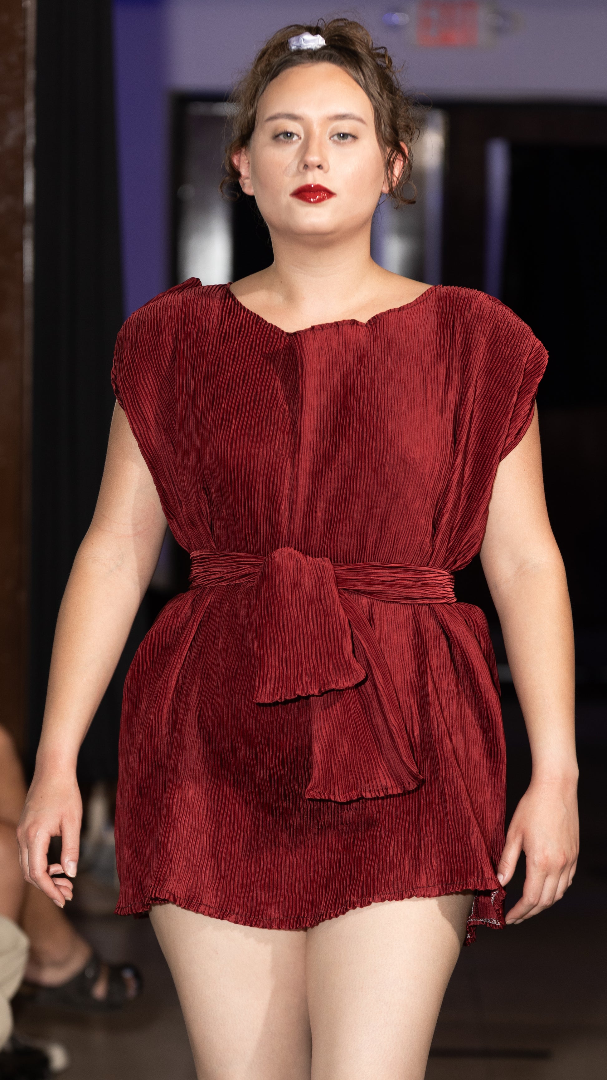This photo shows a size adjustable red pleated mini dress with a waist belt that ties for self tailoring purposes. 