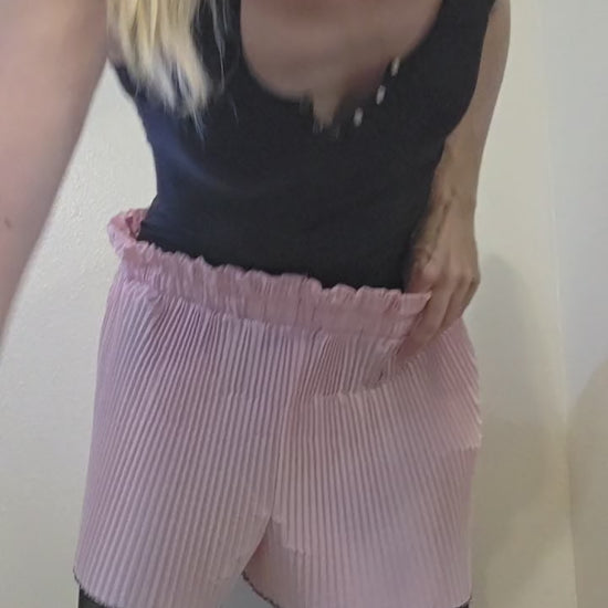 This photo shows a pair of bubblegum pink, pleated shorts with a size- adjustable waistband. 