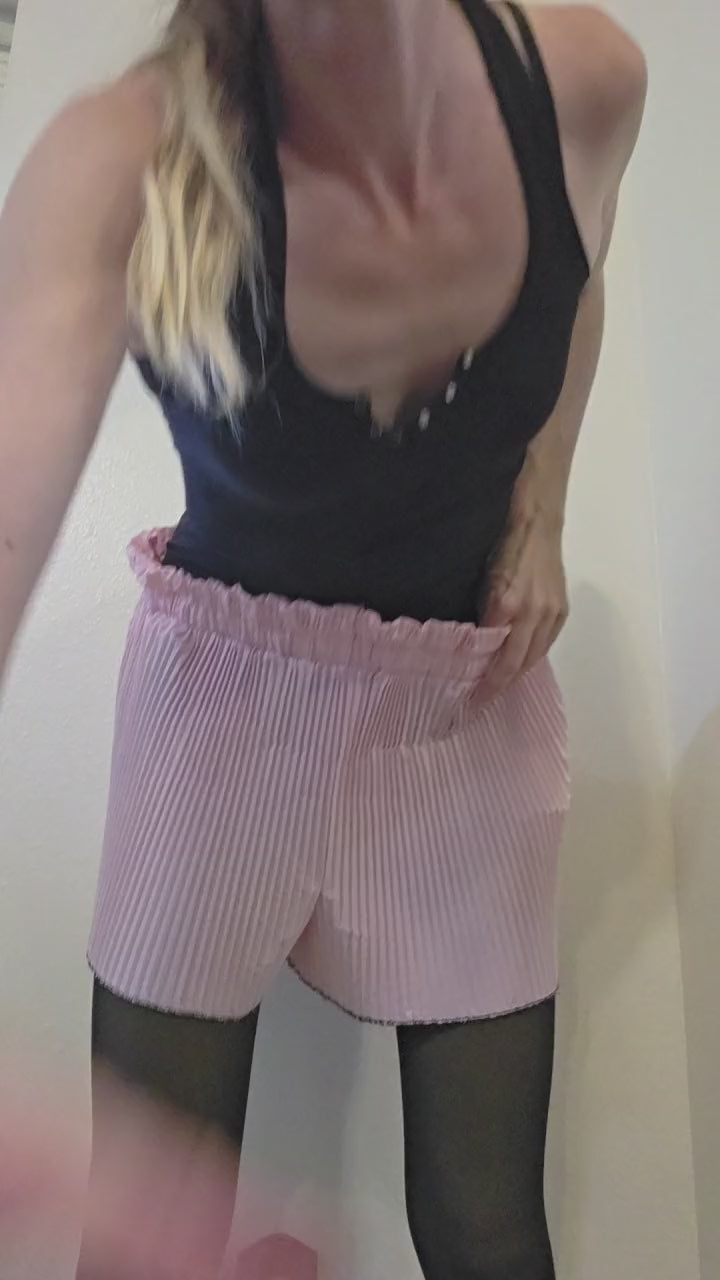 This photo shows a pair of bubblegum pink, pleated shorts with a size- adjustable waistband. 