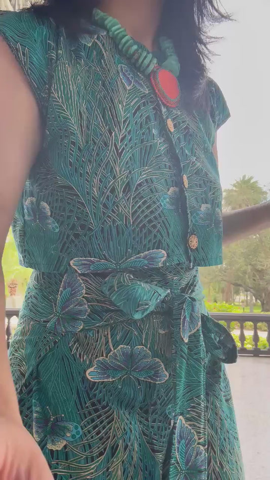 This video shows a model showing off a moth patterned cotton fabric two piece set that is size adjustable by means of a tie waistbelt. The top features a cro top with gold buttons